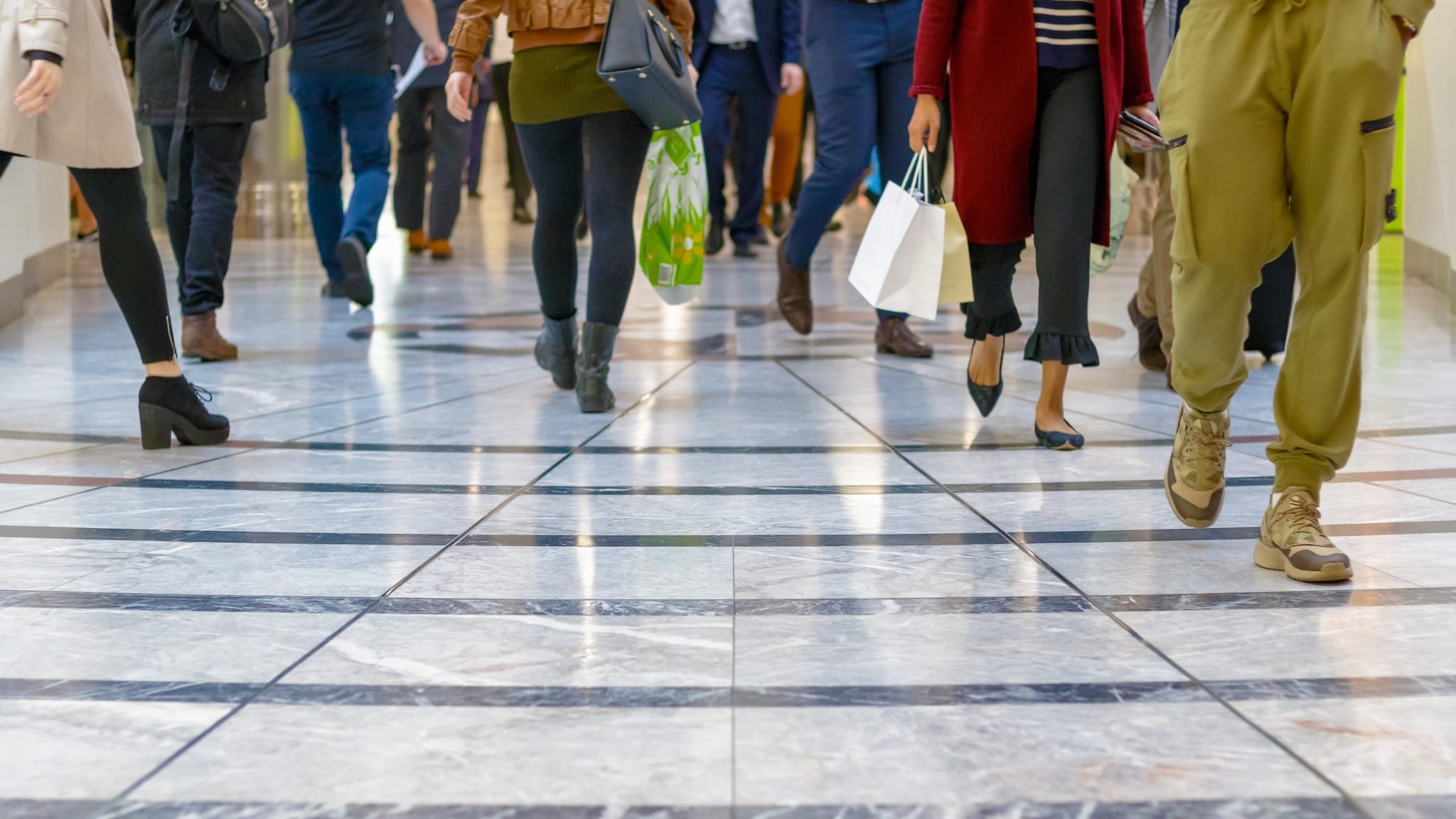 Photo of people's legs as they walk in an indoor shopping mall.