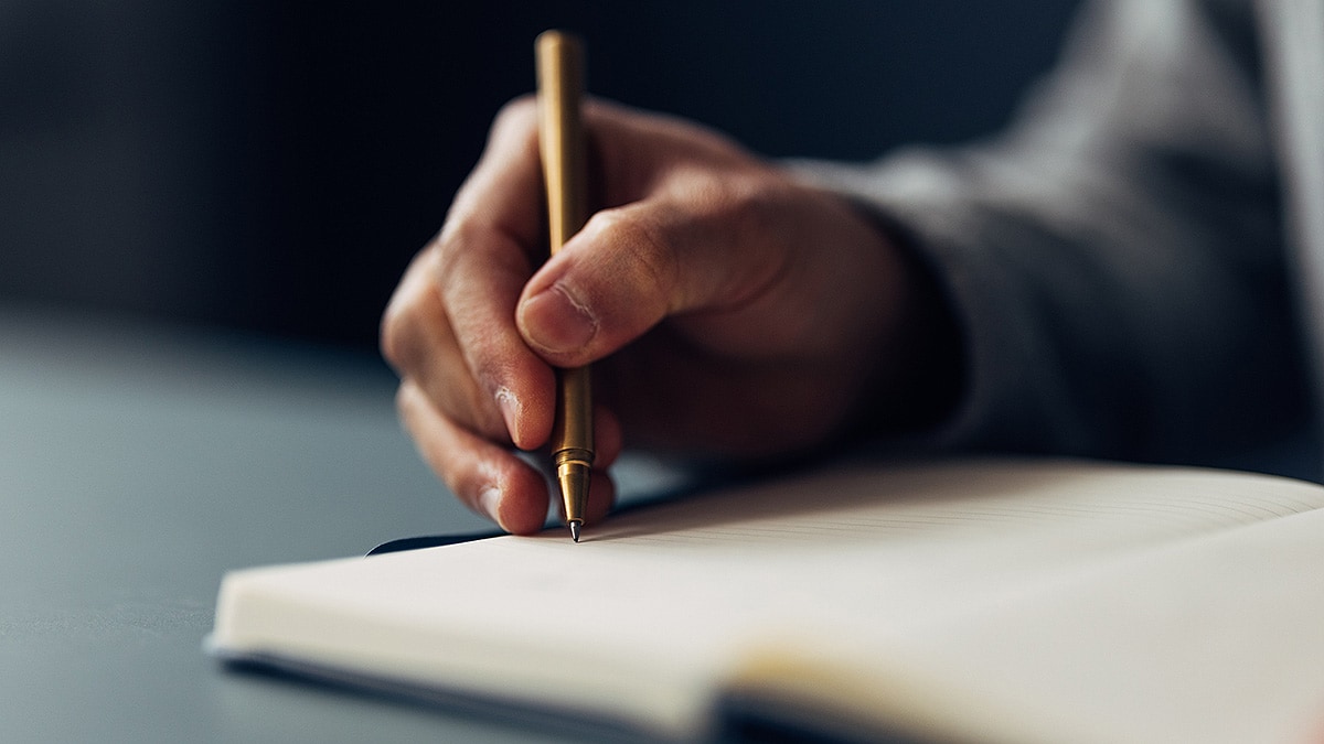 Close up of a person's hand taking notes with a pen and notebook.