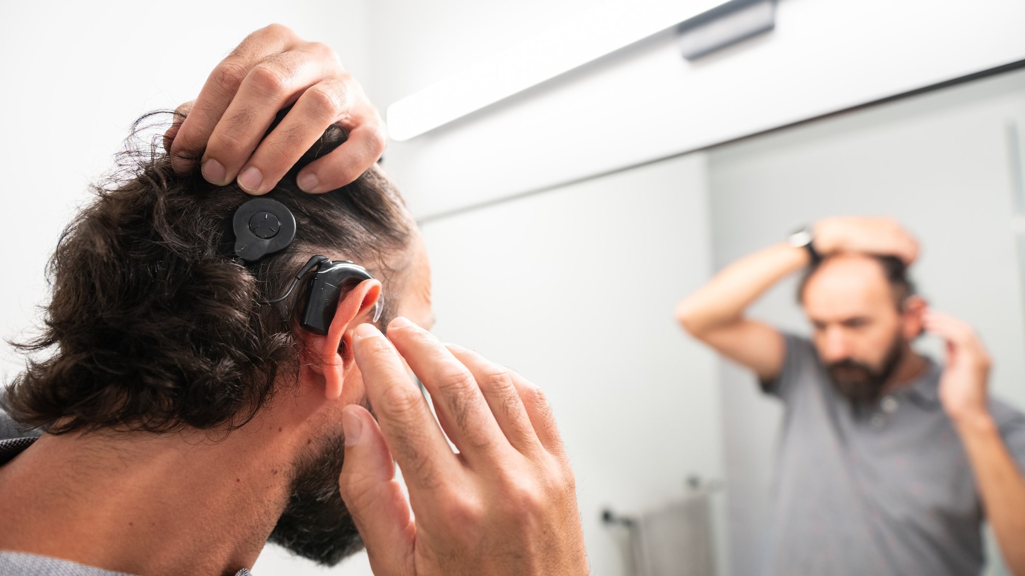 Man adjusting his cochlear implant in the mirror in his home bathroom.