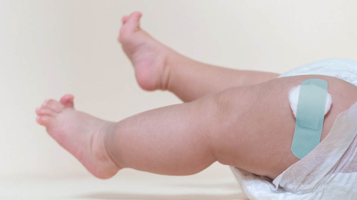Legs of a baby laying down with a Band-Aid on its leg after receiving a vaccine.