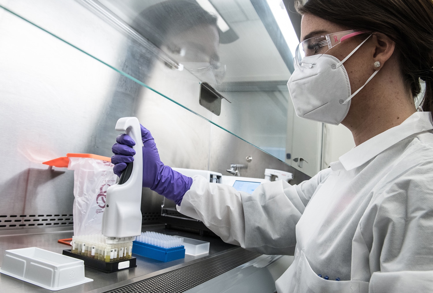 A scientist wearing Biosafety Level 2 PPE gear including gloves, laboratory coat, goggles, and mask, while pipetting inside a Biological Safety cabinet (BSC).