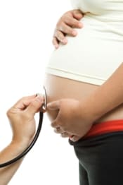 Médico escuchando el estómago de una mujer embarazada con un estetoscopio