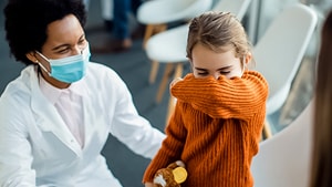 Trabajador de la salud con una mascarilla, clasificando a un niño que tose en la sala de espera de un centro de atención médica.
