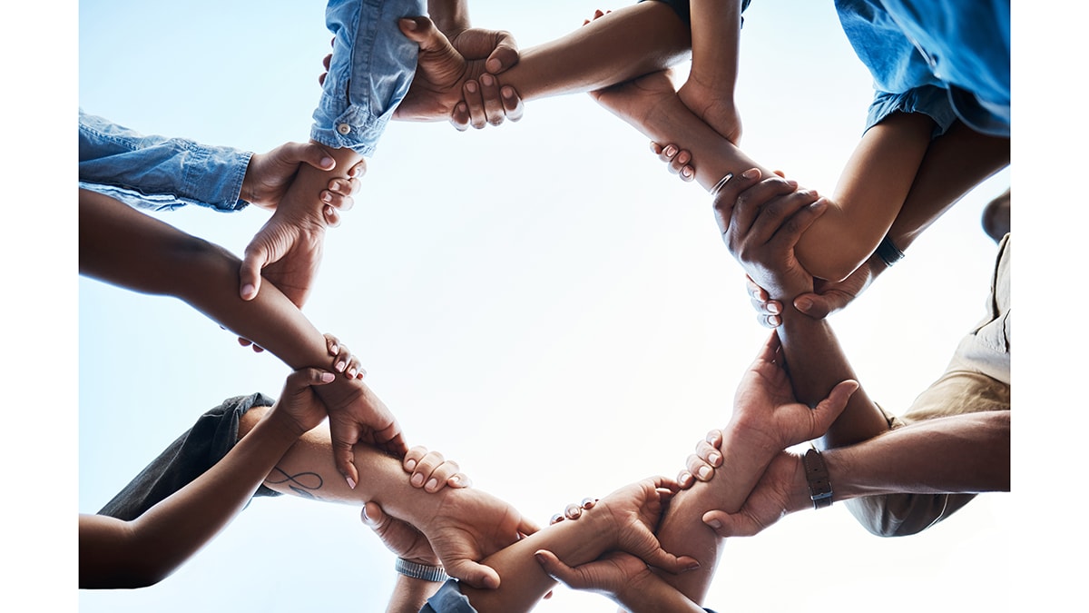 Image, from below, of people linking arms to create a circle.