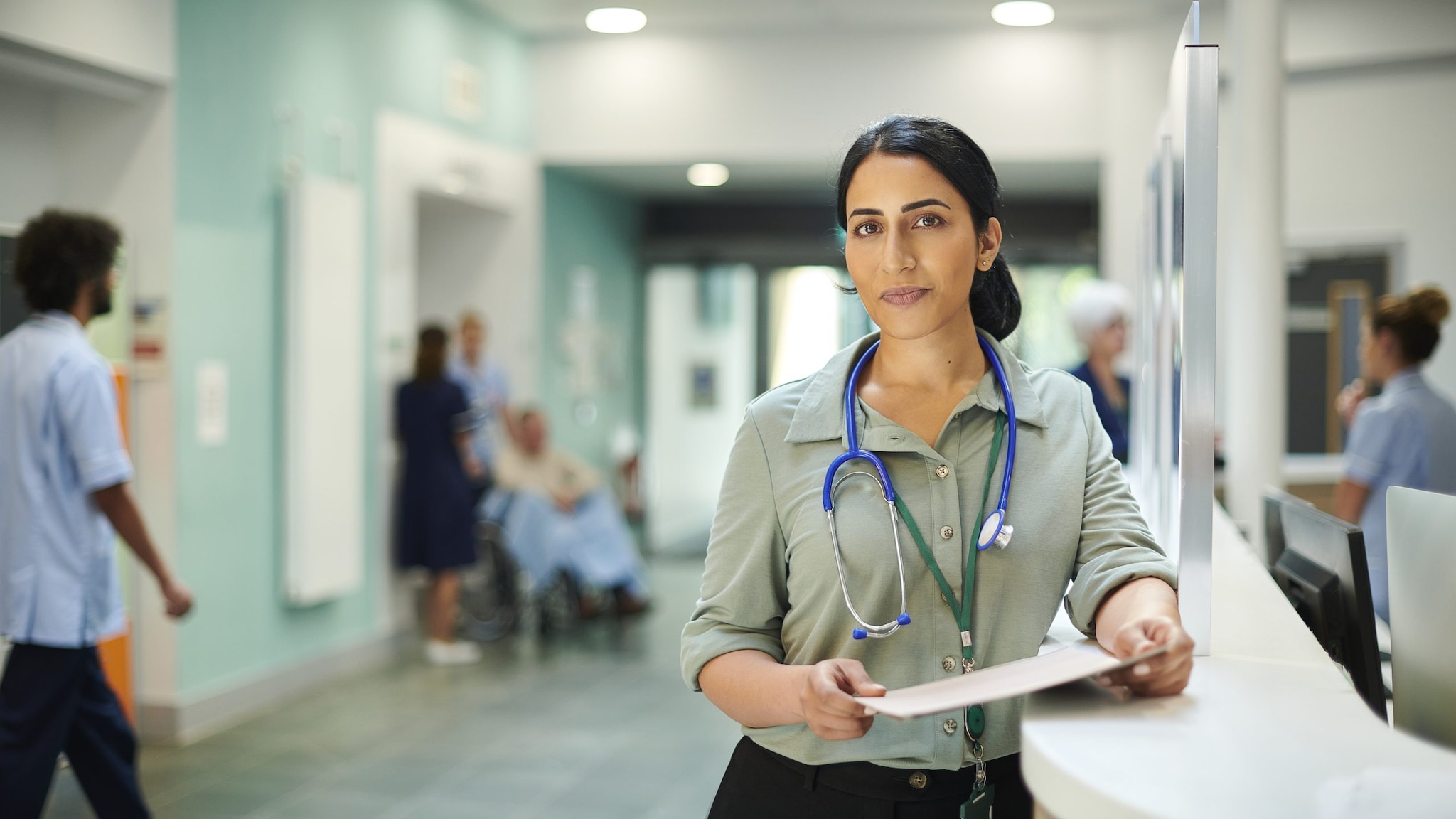 Female doctor stands in medical facility wearing a green shirt and stethoscope
