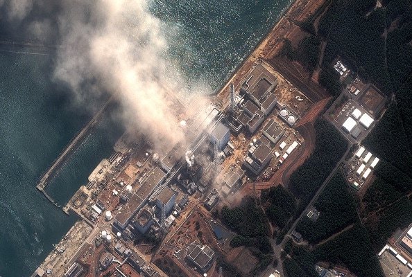 A top-down, aerial view of the Fukushima Daichii nuclear power plant after being damaged by a series of explosions. Smoke is rising from the facility.