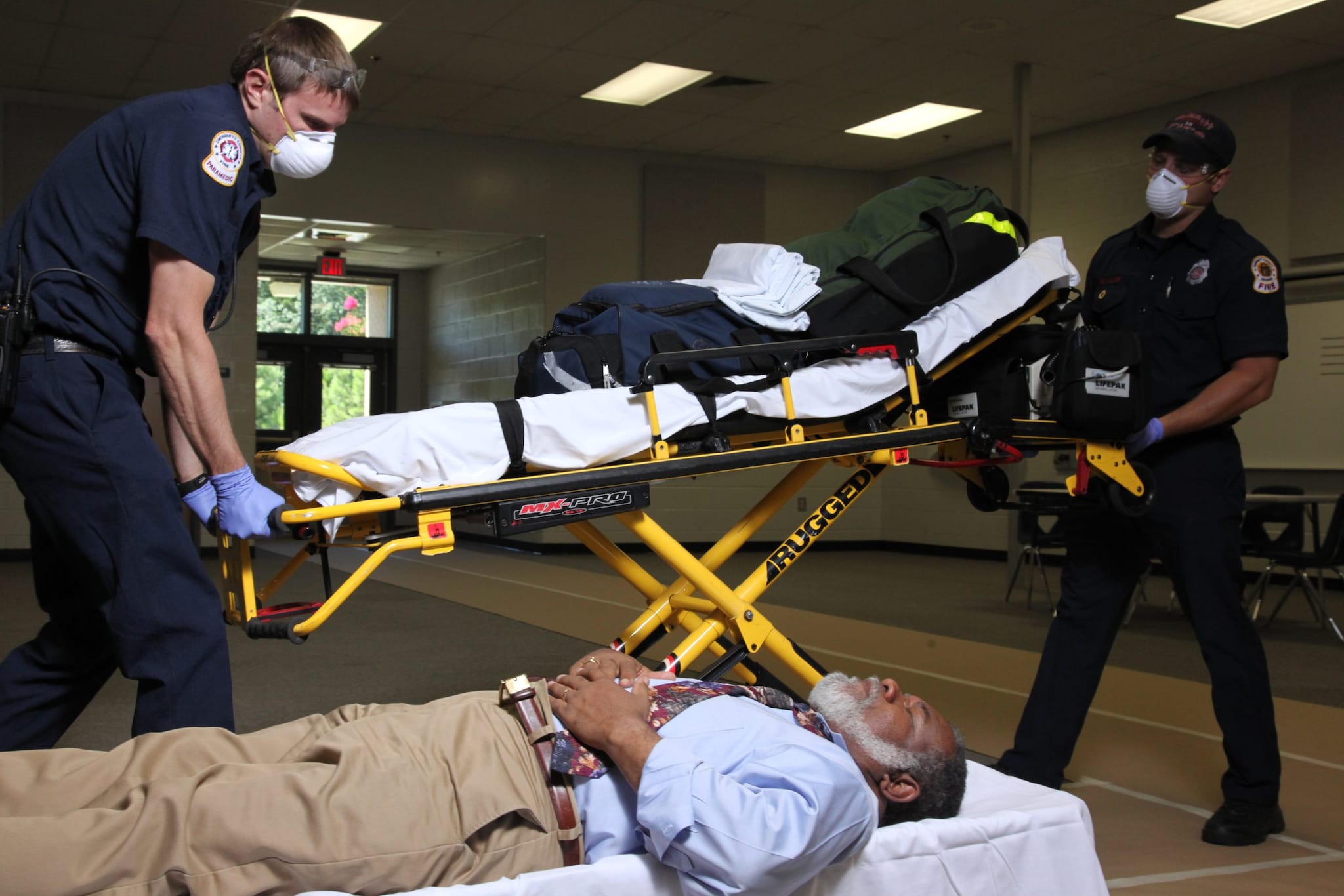 Emergency medical services responding assisting person lying on a cot on the floor inside a community reception center.