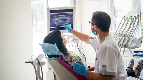 Dentist in an office with a patient. The dentist is point out teeth on an x-ray