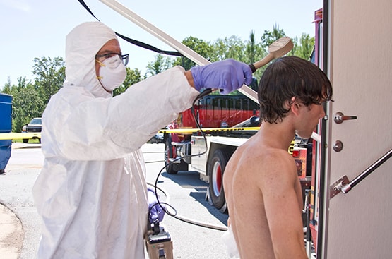A young man being washed at a decontamination station by a suited health worker.