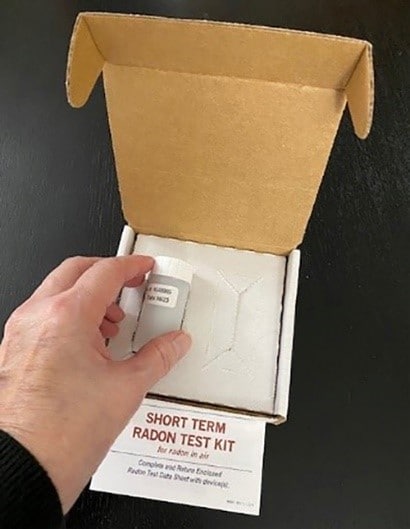 A hand pulls a radon test kit tube from a box