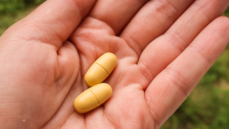 Two pill capsules resting in the palm of an adult hand.