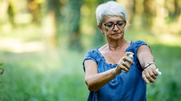 Older woman spraying insect repellent on her arm
