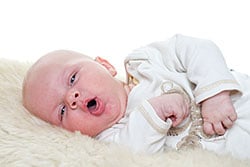 Infant lying down on blanket, coughing.