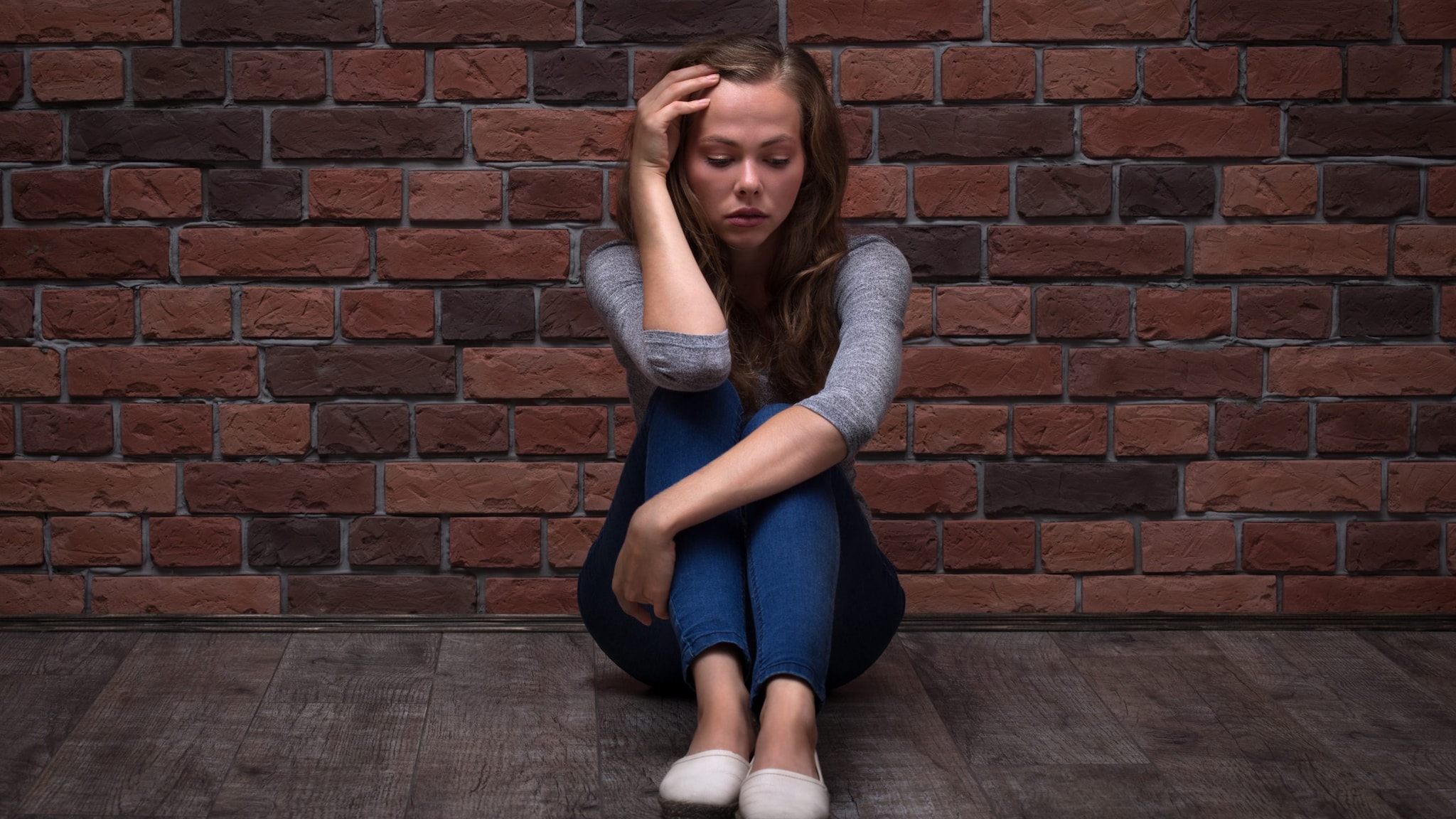 Depressed Teenager Girl Sitting against a brick wall