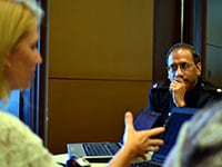 A man listens to a woman speaking at a table filled with laptops.