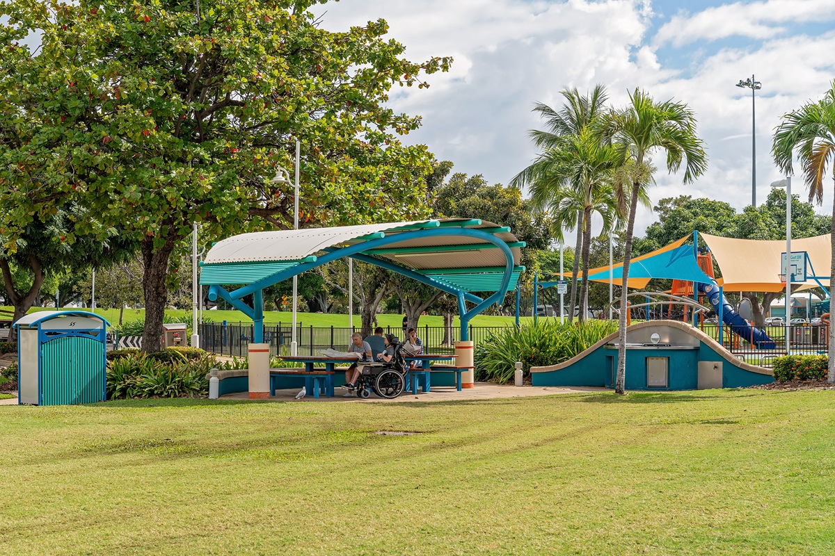 People enjoying an outdoor picnic under a shade structure near a playground in Queensland, Australia