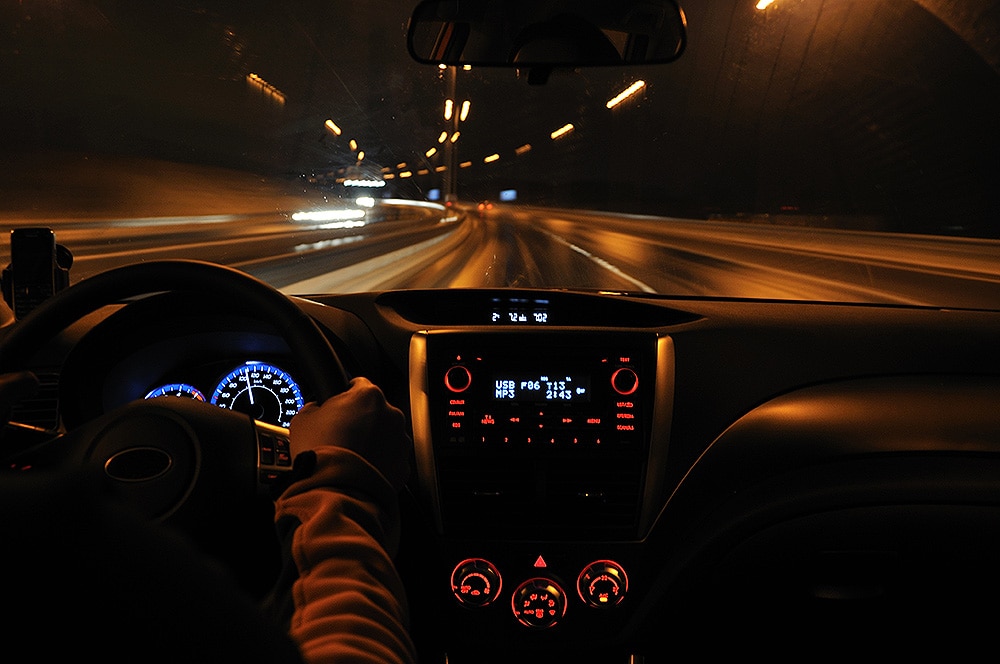 Photo of hands on a steering wheel of a car, driving at night.