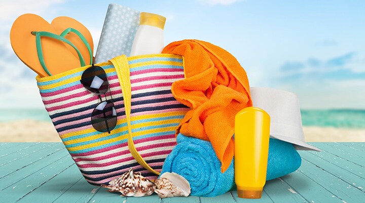Un bolso de mano con unas sandalias, gafas del sol, protector solar, toallas, y un sombrero.