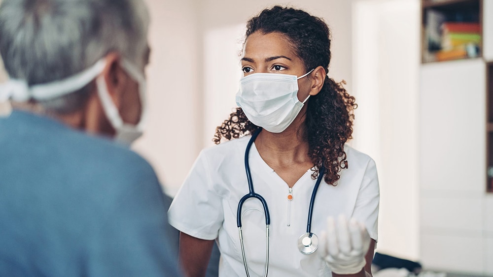 Female doctor talking with a senior patient. Both people are wearing protective face masks