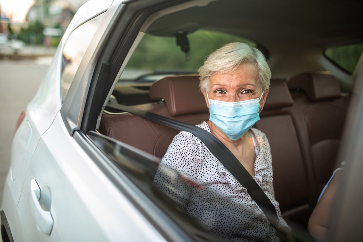 Senior woman wearing protective face mask, sitting on back seat of car during a ride
