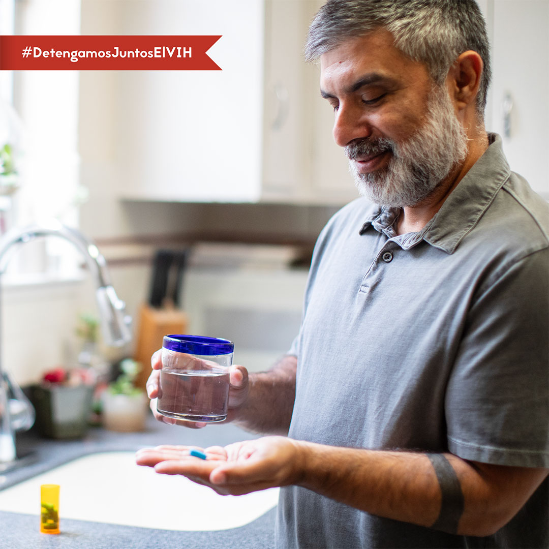 Healthy Aging – Javier (ES) Una imagen de un hombre sosteniendo su píldora de PrEP en una mano y su vaso de agua en la otra mientras está en la cocina.
