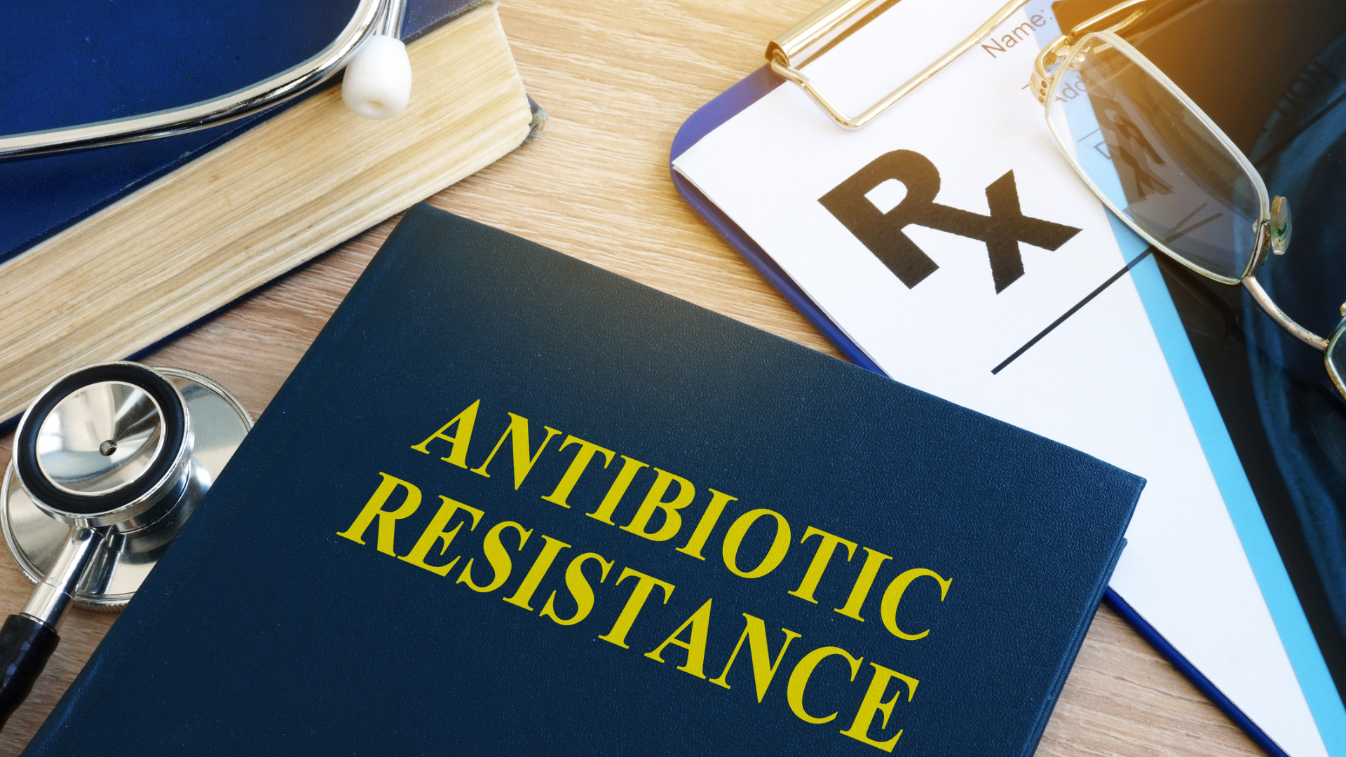 Dark blue book with yellow writing that says Antibiotic Resistance beside a prescription pad and stethoscope