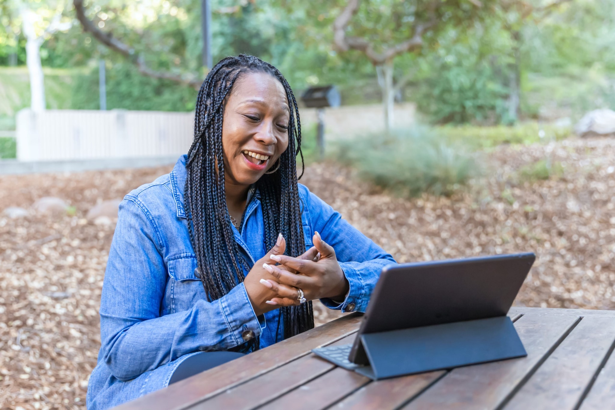 A woman having a conversations with someone virtually on a tablet outside in a park.