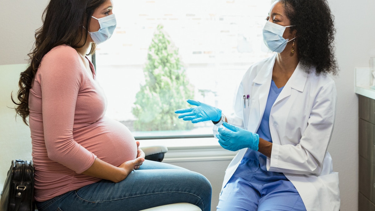 Pregnant patient with healthcare professional. Both are wearing masks.
