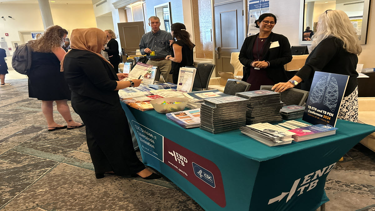 People interacting at a CDC booth with educational materials on TB elimination at a health conference.