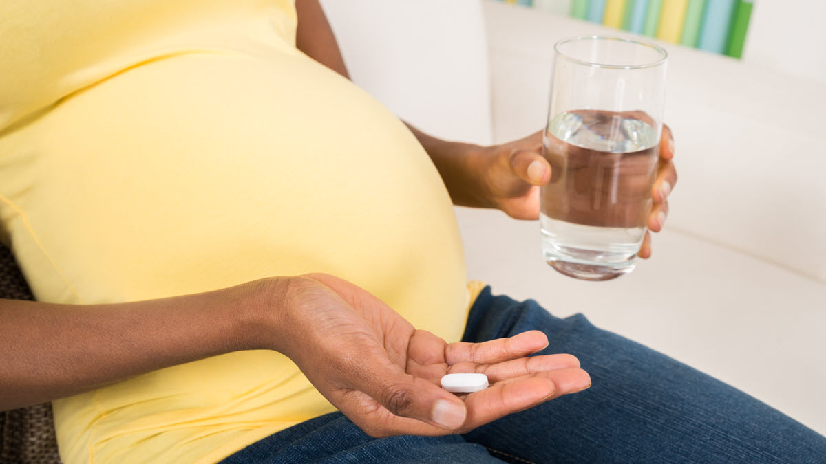 African American pregnant woman holding TB medicine and a glass of water