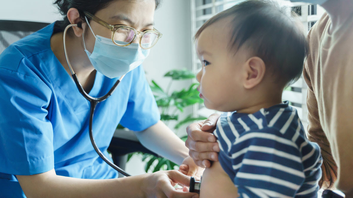Female doctor wearing mask and listening to infant's lungs
