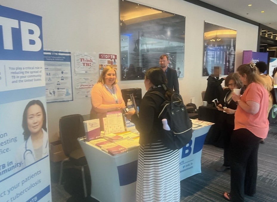 CDC employee standing behind exhibit booth talking to members at the National TB Conference