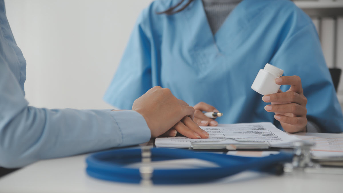 A health care provider holds a bottle of medication while consulting with a patient