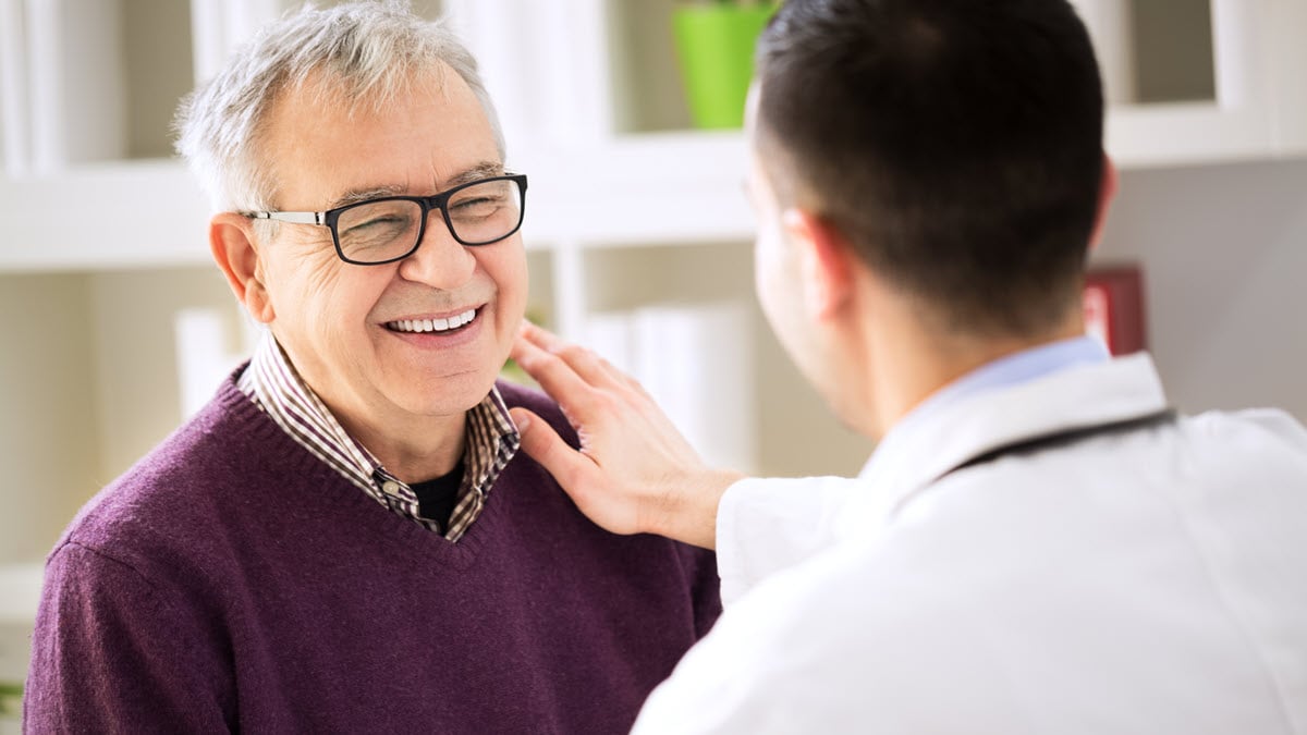 A male patient wearing glasses smiles while speaking with a health care provider