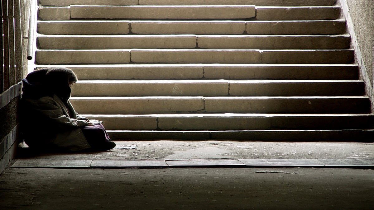 A person experiencing homelessness sitting at the bottom of a staircase