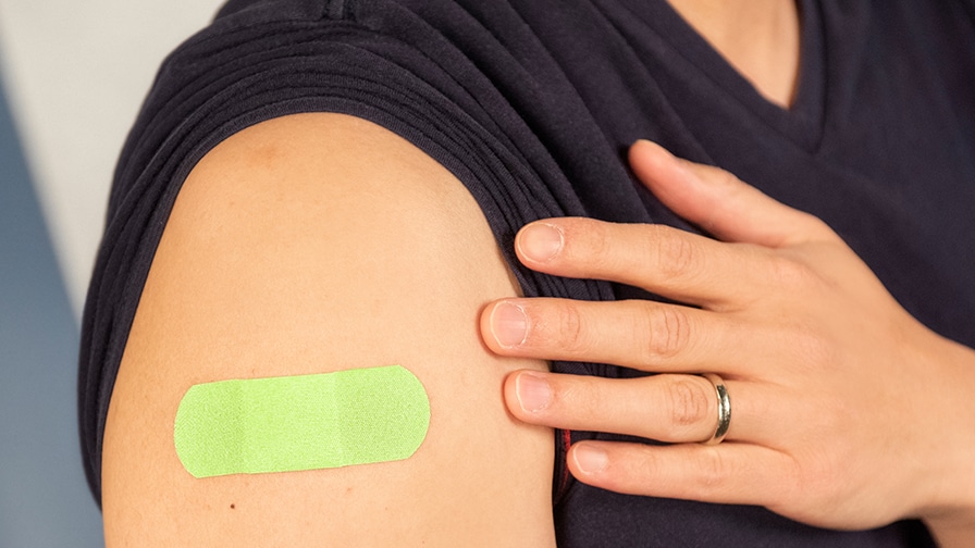 Person shows green bandage on arm after vaccination.