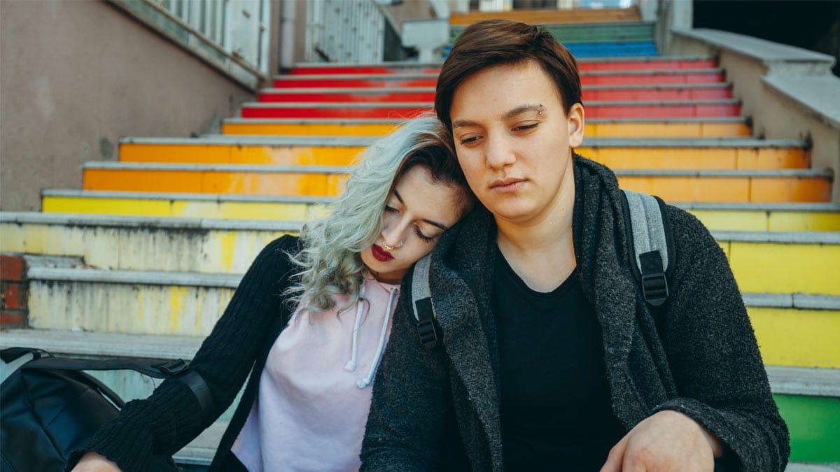Couple sitting at the bottom of stairs with LGBT colors.