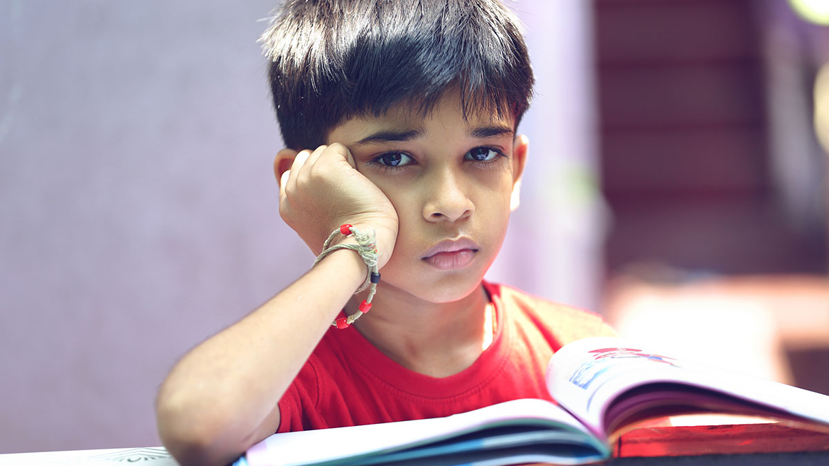 Young boy looking up from a book with a sad face