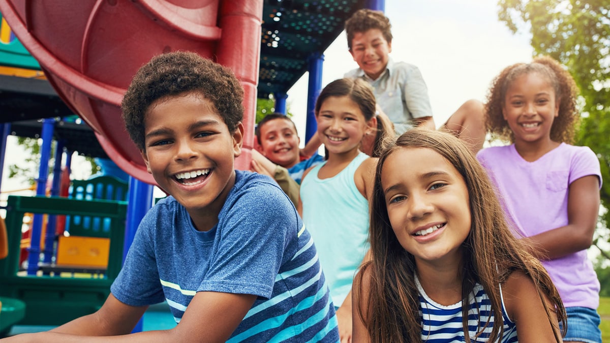 A diverse group of children sit at the bottom of a slide on a playground.
