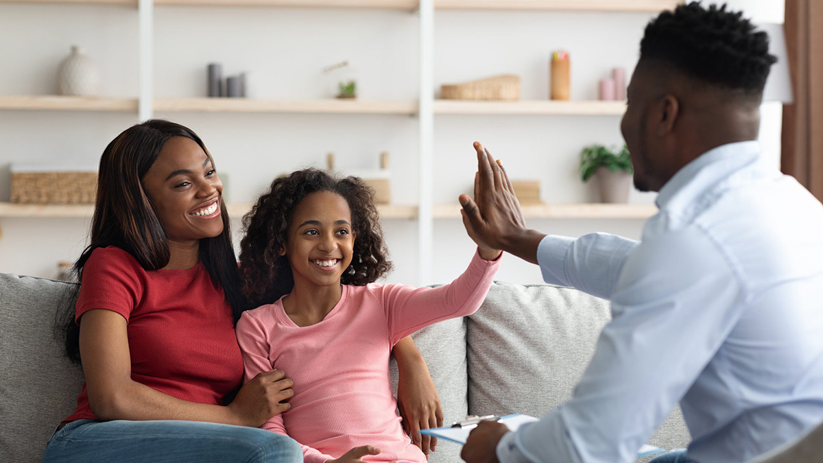 Therapist gives a high-five to a young patient while her mother sits beside her.