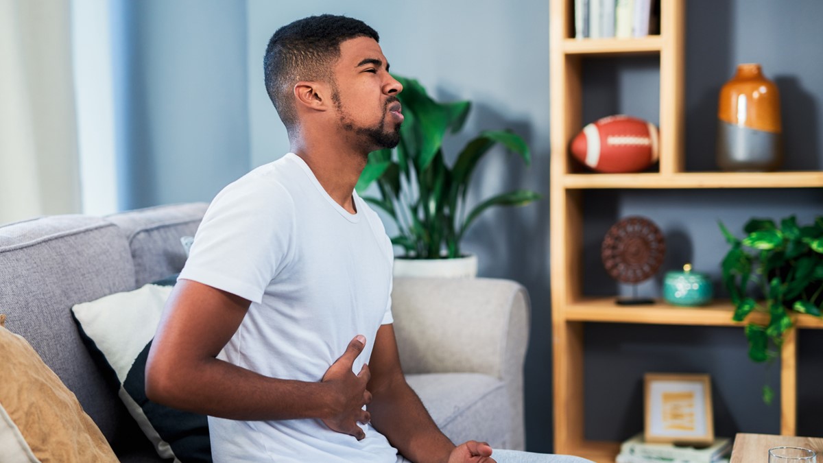 A young man on a couch holds his stomach owing to pain.