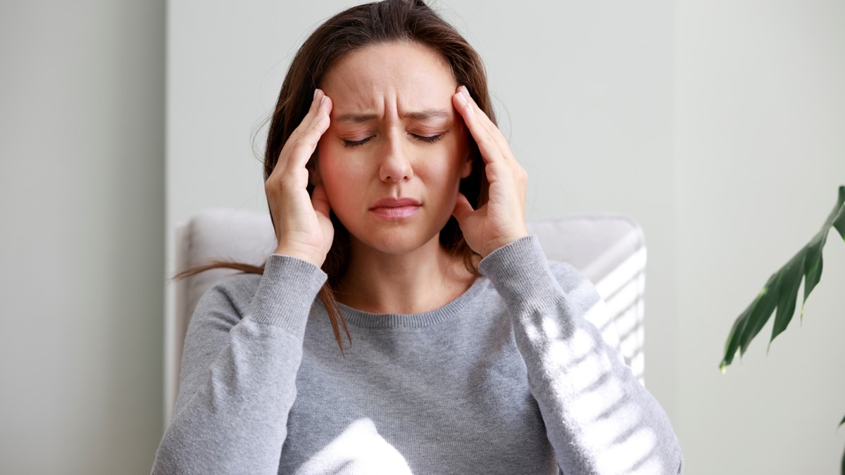 A woman holds her head and closes her eyes in pain.