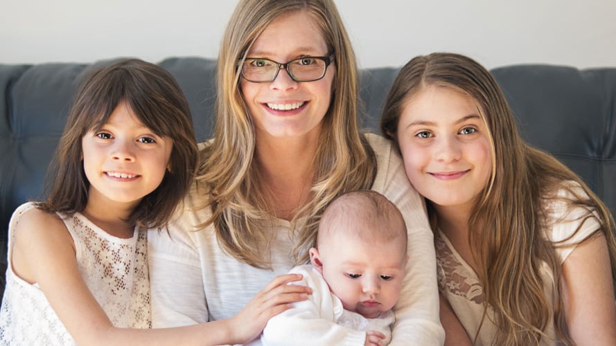 A mother sits on a couch holding an infant with two of her other children on each side of her.