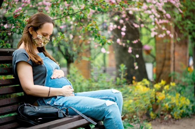 Pregnant woman sitting on a bench looking at her belly and holding it with her hands