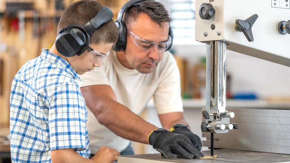 Man and young boy both wear eye protection while working with band saw
