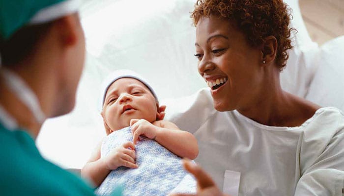 Una madre sonríe mientras sostiene en brazos a su bebé recién nacido en el hospital.