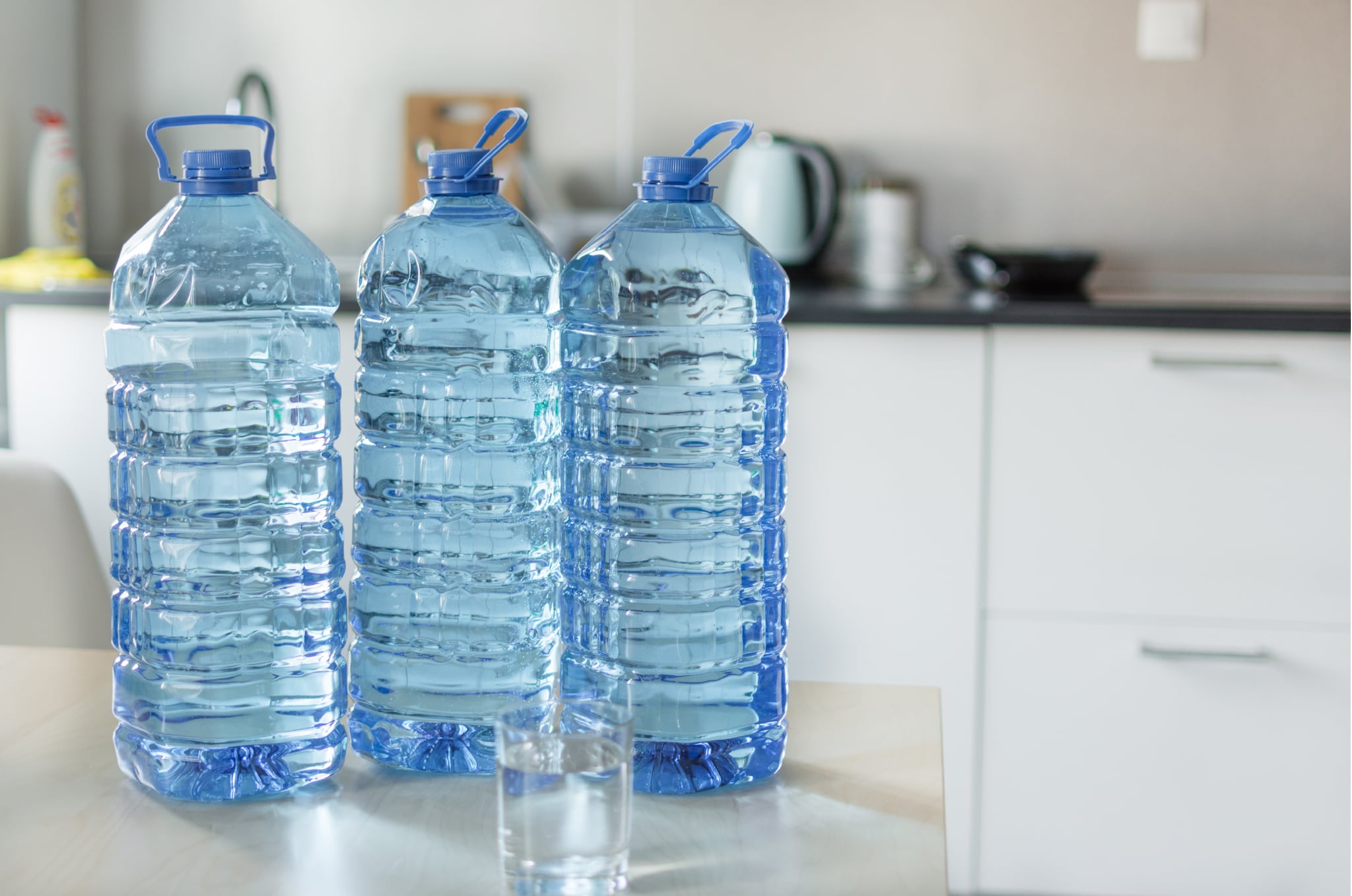 Foto de tres botellas grandes transparentes con agua sobre la mesa con un trasfondo de cocina.