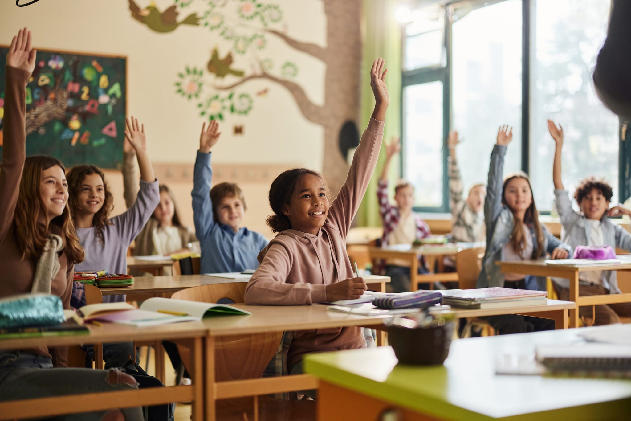 Happy elementary school students raising their hands during a class.