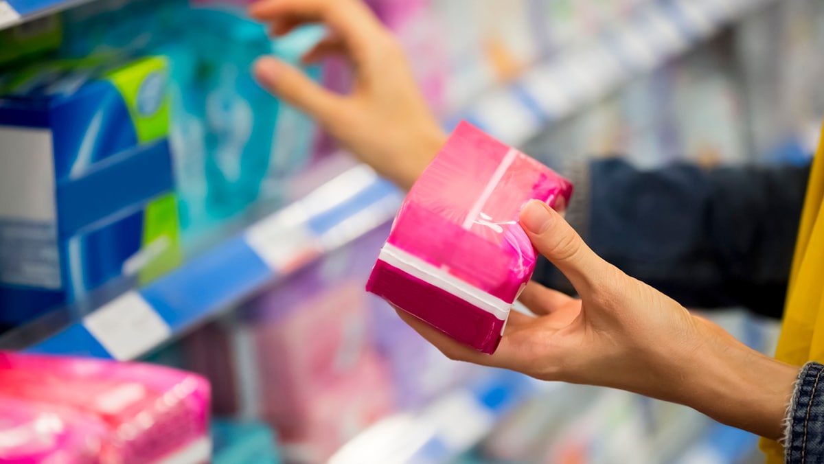 Woman picking up menstrual hygiene products from store.