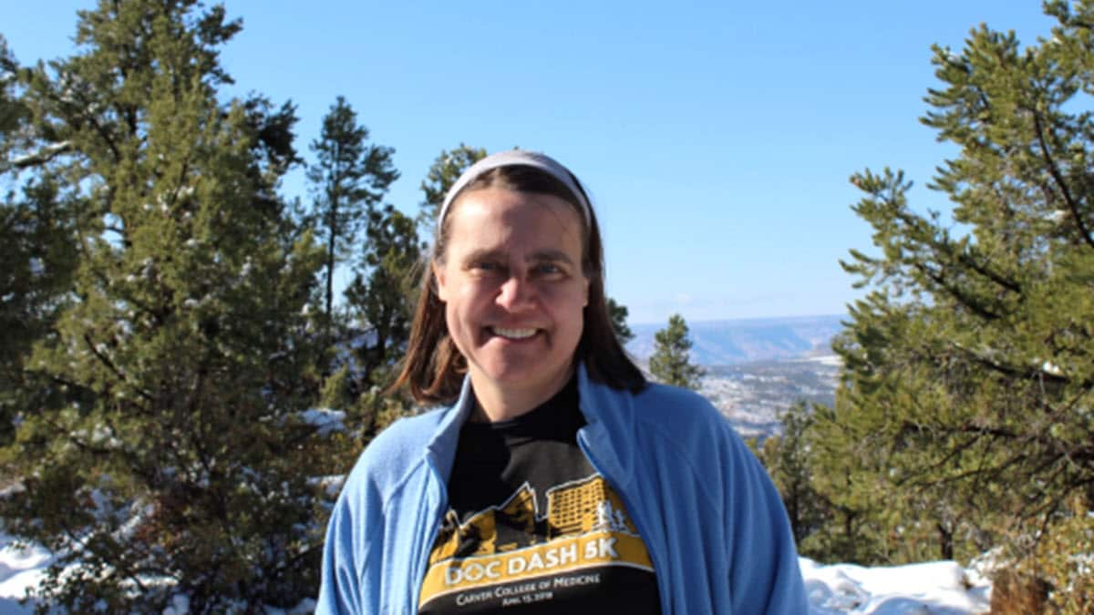 TB Champion Cecilia Norris wearing a blue jacket smiling outside in front of trees and snowy mountains